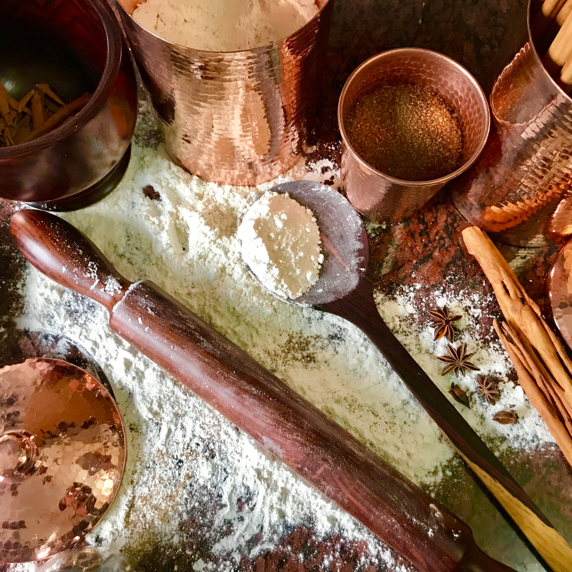 Beautiful copper jars holding fresh cinnamon sticks, sugar and flour, and granadillo dar red wood roller, large spoon and mortar and pestle crushing cinnamon sticks