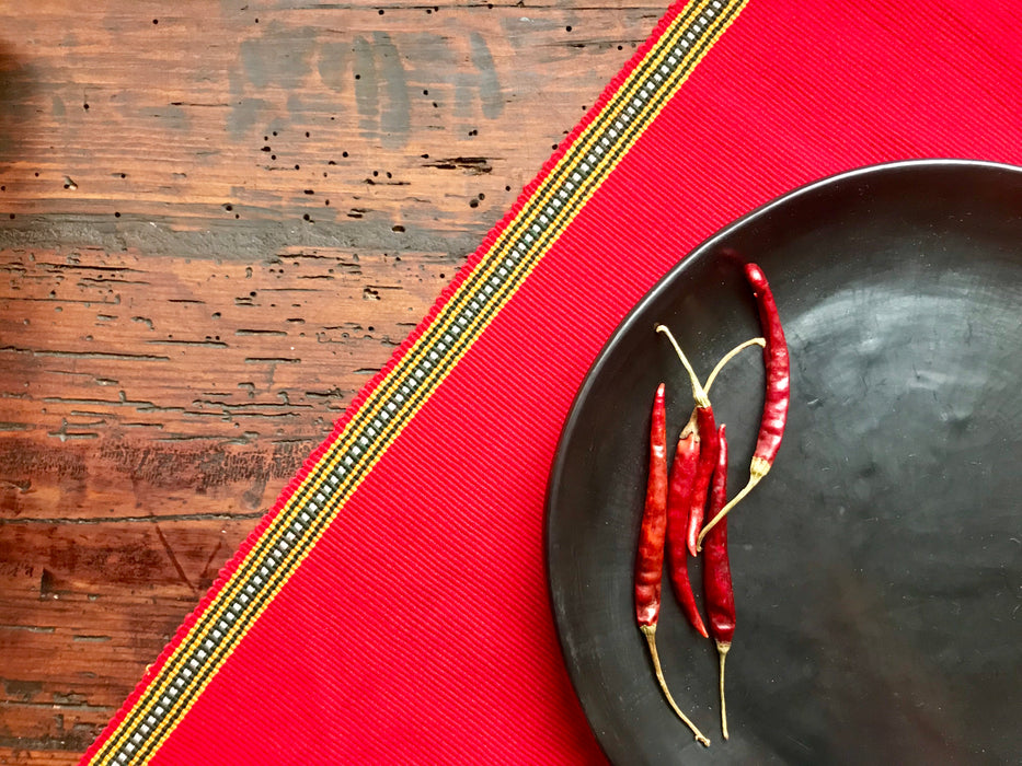 Mexico 1492 - bright red table cloth with colorful edges, handmade on a backstrap loom in Chiapas Mexico. Paired with Black Clay plate from the same shop
